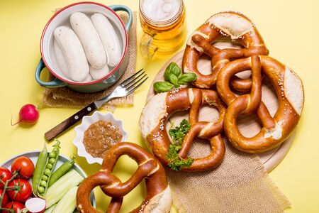 Pretzels, white bavarian sausages, mustard and beer, german traditional food, oktoberfest on yellow backgroundの写真素材