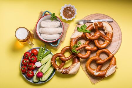 Pretzels, white bavarian sausages, beer, mustard and vegetables on yellow background, german traditional food, oktoberfestの写真素材