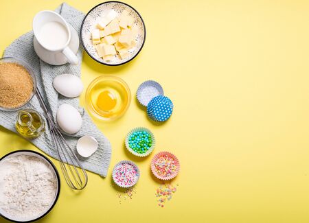 Baking ingredients for cake, cupcakes or muffins on yellow copy space background for text, sugar pearls, eggs, whisk, flour, butter, sugar and milkの写真素材