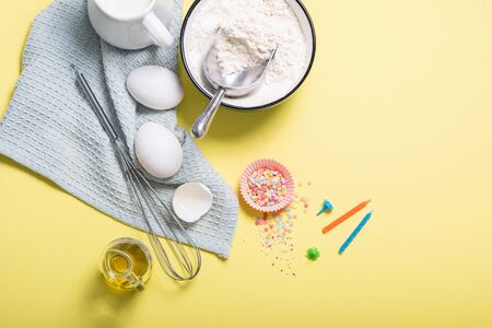 Baking ingredients for birthday cake, cupcakes or muffins on yellow background, sugar pearls, whisk, flour for doughの写真素材