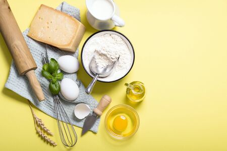 Cooking ingredients for pasta, flour, parmesan cheese, basil, eggs, rolling pin and olive oil, top view, italian cooking, yellow background copy spaceの写真素材
