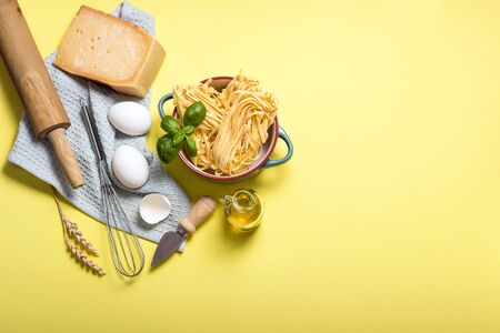 Uncooked pasta, ingredients for cooking, parmesan cheese, eggs, rolling pin and olive oil, italian cooking, yellow background copy spaceの写真素材