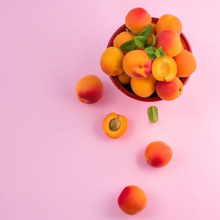 Ripe apricots in a bowl on pink paper background copy space, summer fresh fruits, vitamins, top viewの写真素材