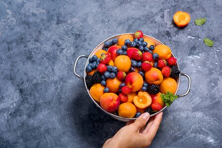 Hand holding colander with fresh summer fruits and berries, apricots, blueberries, strawberries, copy space backgroundの写真素材