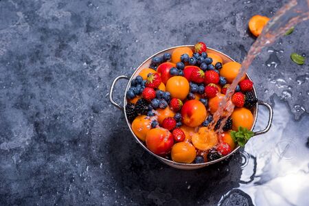 Water splashing on fresh summer fruits and berries, apricots, blueberries, strawberries in colander, washing fruits and berries, healthy eating, vegan foodの写真素材