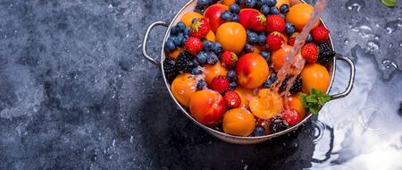 Water splashing on fresh summer fruits and berries, apricots, blueberries, strawberries in colander, washing fruits and berries, healthy eating, vegan food, copy space backgroundの写真素材