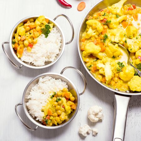Vegetarian curry with cauliflower and chickpeas served in metal bowls with rice, healthy homemade vegan food, indian cuisine, clean eating concept, square imageの写真素材