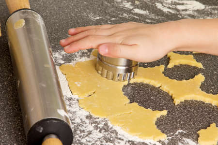Hand with a cookie cutter in pastry and a rolling pin on a kitchen worktop