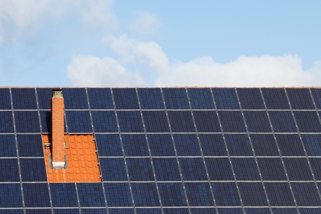 Many solar panels around a chimney on a roof