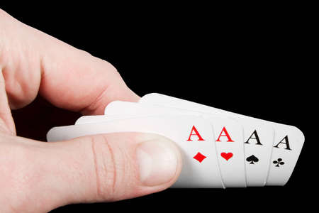 Hand with four playing cards showing aces over a black background