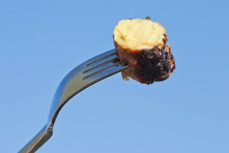 Fork with grilled sausage and mustard in front of a blue skyの写真素材