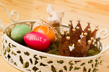Easter basket with moss colorful eggs a bunny and two burning tealights in front of a wooden backgroundの写真素材