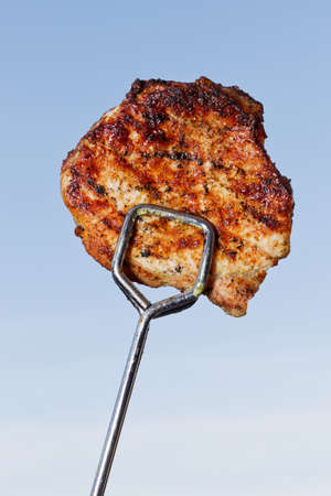 Grilled steak in pliers in front of a blue sky with cloudsの写真素材