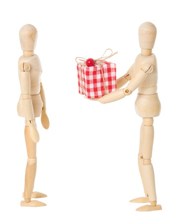 A wooden doll gives a red present to another wooden doll over a white backgroundの写真素材