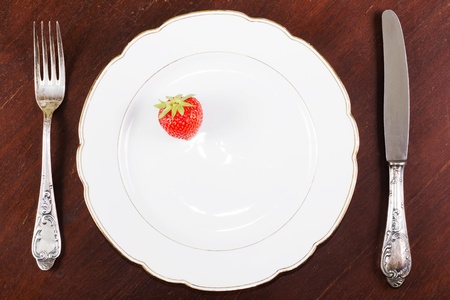 White plate with a strawberry and a fork and a knife on a wooden tableの写真素材