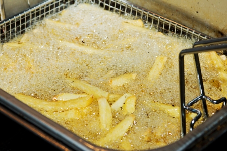 Closeup of many french fries in hot fat in a deep fryer