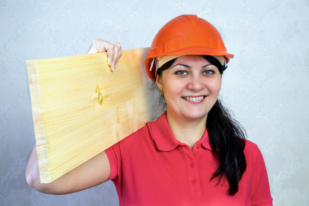 Girl the builder in a helmet with a plank of wood. Close portrait of a smileの写真素材