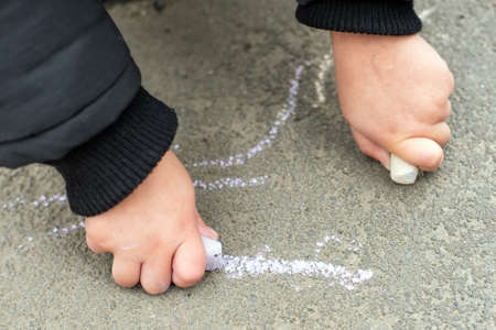 A boy in a jacket draws chalk on the asphalt in the autumn on the streetの写真素材