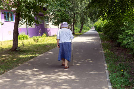 An elderly woman with a cane walks around the city.