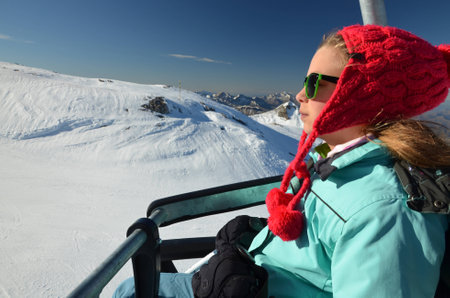 Young girl with red winter hat and sun glasses on chair lift at ski resort Pierre St Martin in...