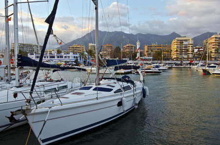 Marbella city harbor seen from the coastal mountain range and cloudy sky in sunset lights are at background foreground is sailing yacht Costa del Sol Andalusia Spainの写真素材