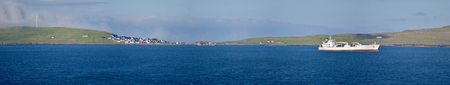 Panoramic view of Nolsoy island in Faroe archipelago village, Atlantic ocean waters and navigating boat are at foregroundの写真素材