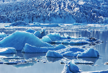 Small Ice-bergs drifting in the water surface of Fjallsarlon Glacier Lake bordered by the wall of...
