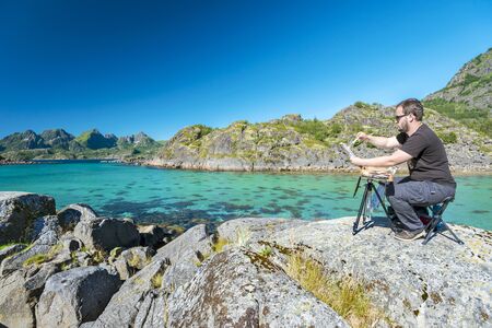 Lofoten, Norway, August 4, 2017 Painter is drawing the picture of the beautiful landscape of Lofoten archipelago from the southern cape of Arsteinen island.のeditorial素材