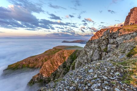 Cliffs of Northern Cape of Soroya Island in midnight sun light. Fascinating sea of clouds is covering the Arctic Ocean surface at the background. Finnmark, Norway.の写真素材