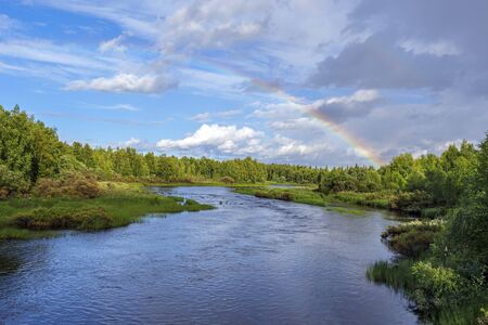 The flow of Kasmanjoki river bordered by pine forests in Finnish Lapland. The sky with rainbow is at background. Picture is taken from E63 Kuusamo road bridge.の写真素材