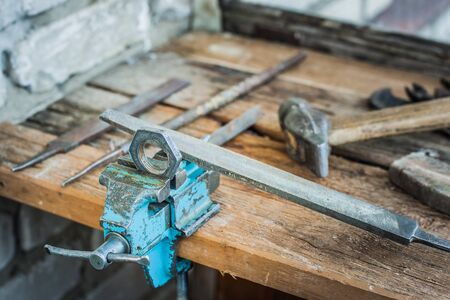 Old workshop in the house. Machining a workpiece clamped in a vise. Old tools on a wooden table.の写真素材