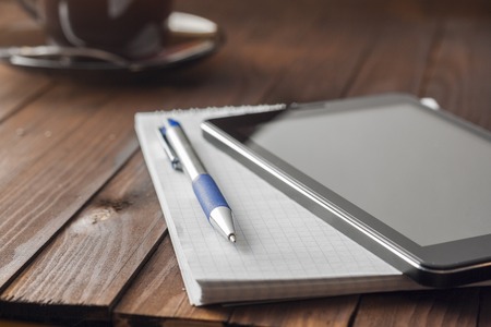 Tablet computer is on notepad with a pen, standing next to a cup of coffee.の写真素材