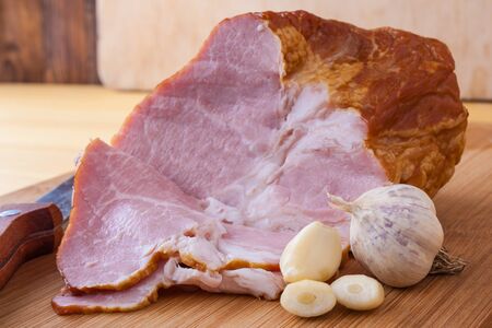 Boiled, smoked pork meat, pork neck, garlic and a knife on a cutting board.の写真素材