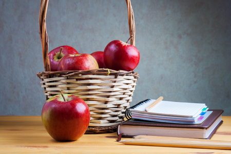 Notebook with a pencil and a basket with apples are on the table.の写真素材