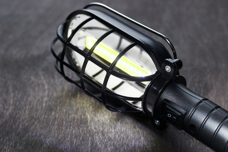 A black portable lamp glows on a wooden table.