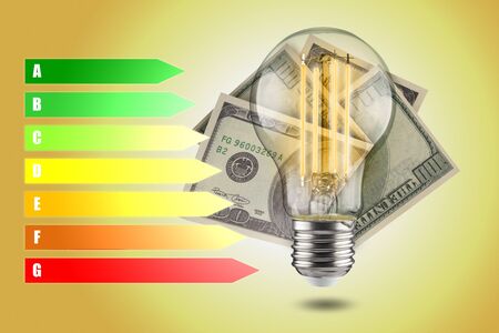 Energy efficiency concept of LED lamps. Decrease in electricity consumption. LED light bulb with dollars on a yellow background.の写真素材