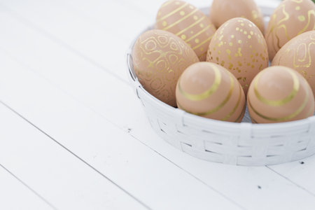 Easter still life. Easter eggs in brown color with a golden pattern in a white basket on a white...