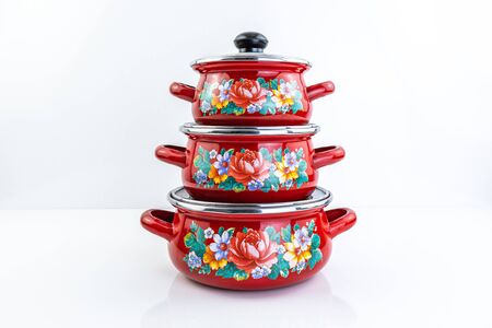 Stainless steel red pots on white background. Set of three stacked cooking pots with glass see...