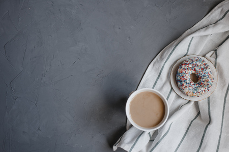 top view on Cup of coffee, a donut and a dish towel on the dark grey background