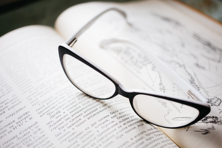 glasses in black and white frame lie on the open book