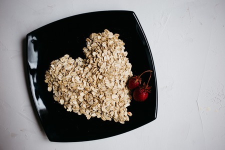 top view oat flakes in the form of a heart on a black plate and fresh strawberriesの写真素材