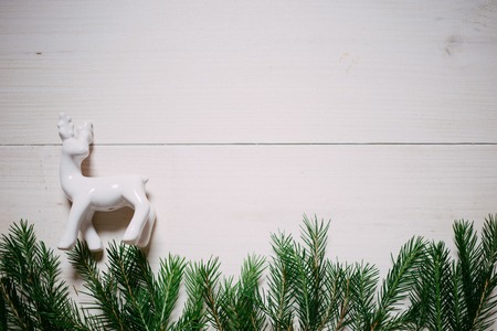 Christmas composition. Christmas gift, white porcelain deer, fir branches on wooden white background, copyspaceの写真素材