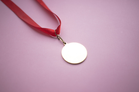 gold medal on a red ribbon on a pink background