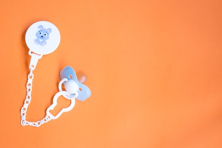 baby blue pacifier with a pin on a orange background, copy space