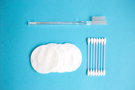 top view personal care products. white bottle, razor, ear sticks, cotton pads, toothbrush on blue...