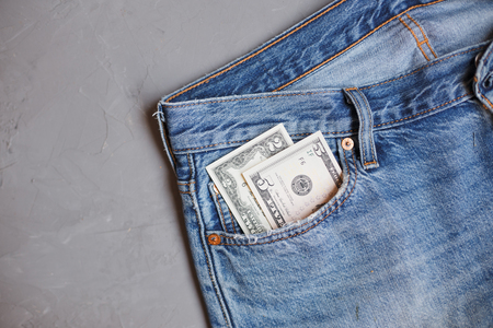 Moscow, Russia - 08 30 2018: Money financial concept. Two and five dollars banknotes in a pocket of blue jeans on gray background.の写真素材