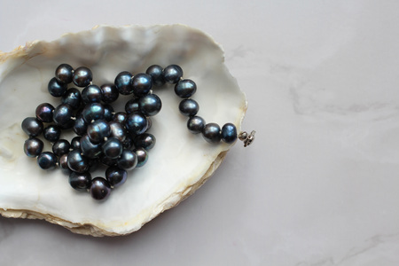 Macro photograph of black pearl beads with precious stones on a shell, marble backgroundの写真素材