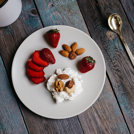 a plate with cottage cheese, strawberries and nuts, a cup of coffee and towels on a wooden table, healthy food, breakfastの写真素材