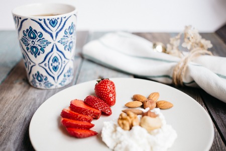 a plate with cottage cheese, strawberries and nuts, a cup of coffee and towels on a wooden table, healthy food, breakfastの写真素材