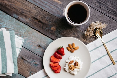 a plate with cottage cheese, strawberries and nuts, a cup of coffee and towels on a wooden table, healthy food, breakfastの写真素材